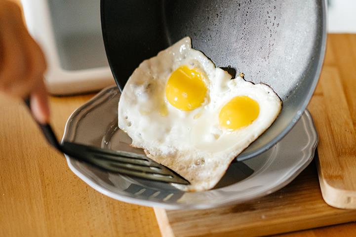 two sunnyside up eggs sliding from a frying pan onto a plate
