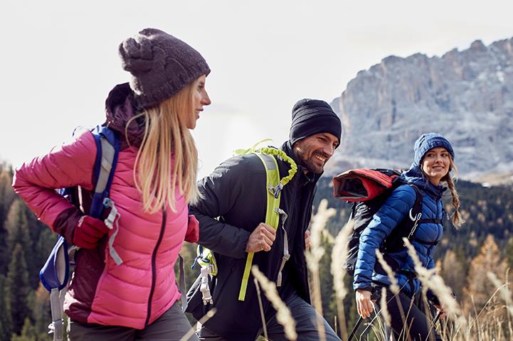 two women and man wearing jackets hiking in mountains